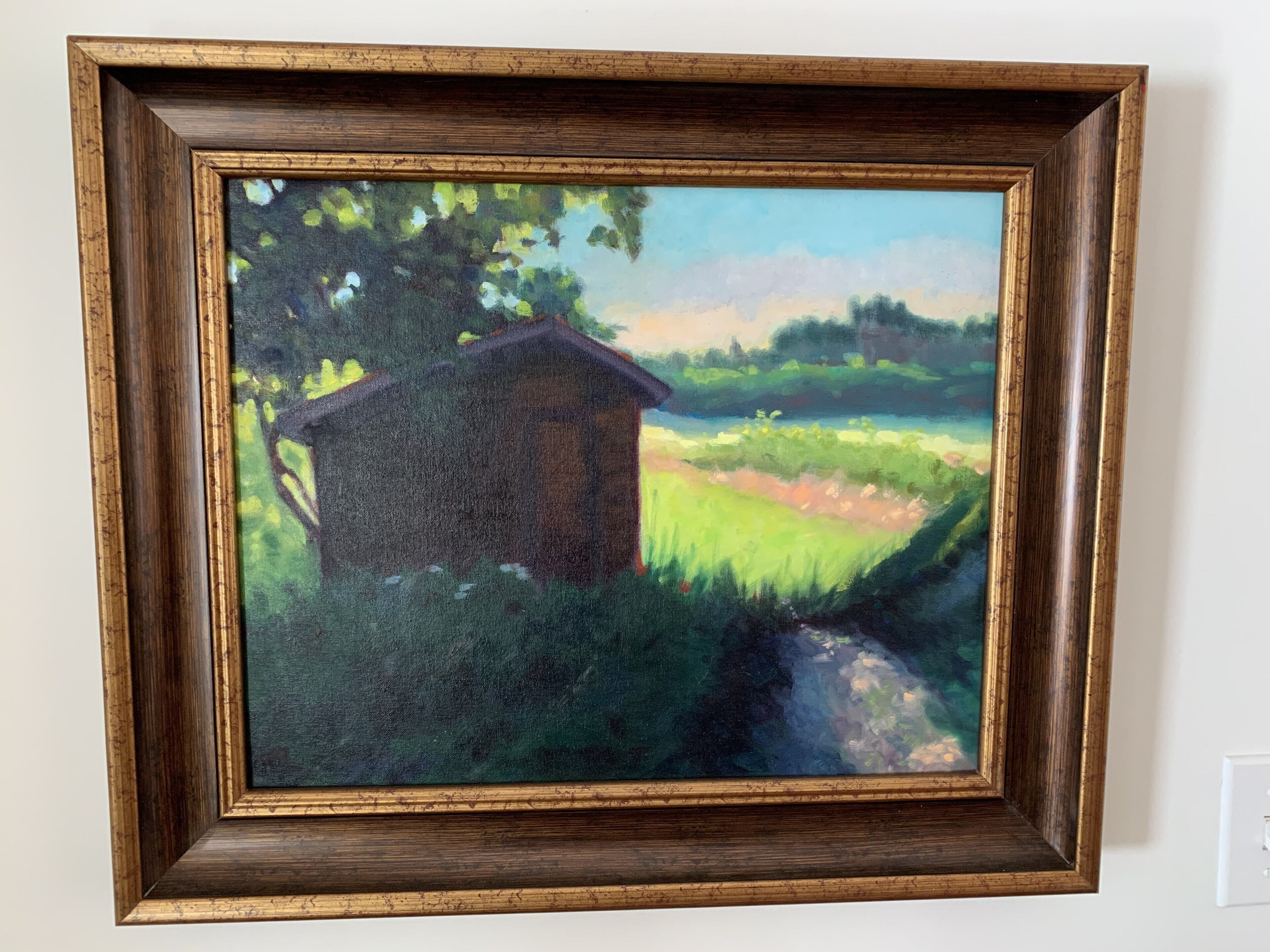 Un cuadro enmarco de una escena campestre con una casa y follaje.
