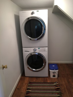 A front-loading washer and dryer stacked in a corner with a wooden floor and a striped rug.