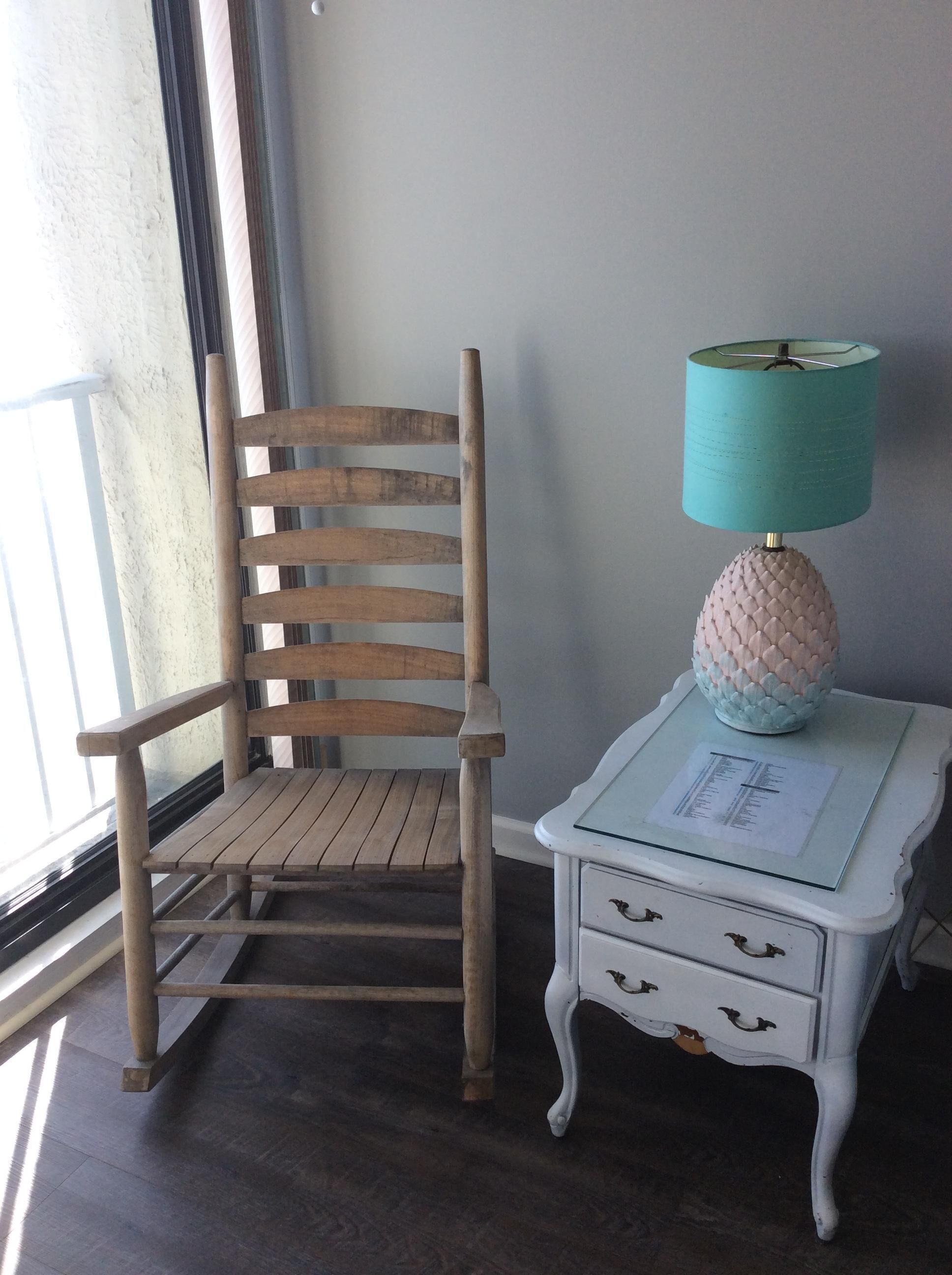 A wooden chair next to a small white nightstand with a lamp and a drawer.
