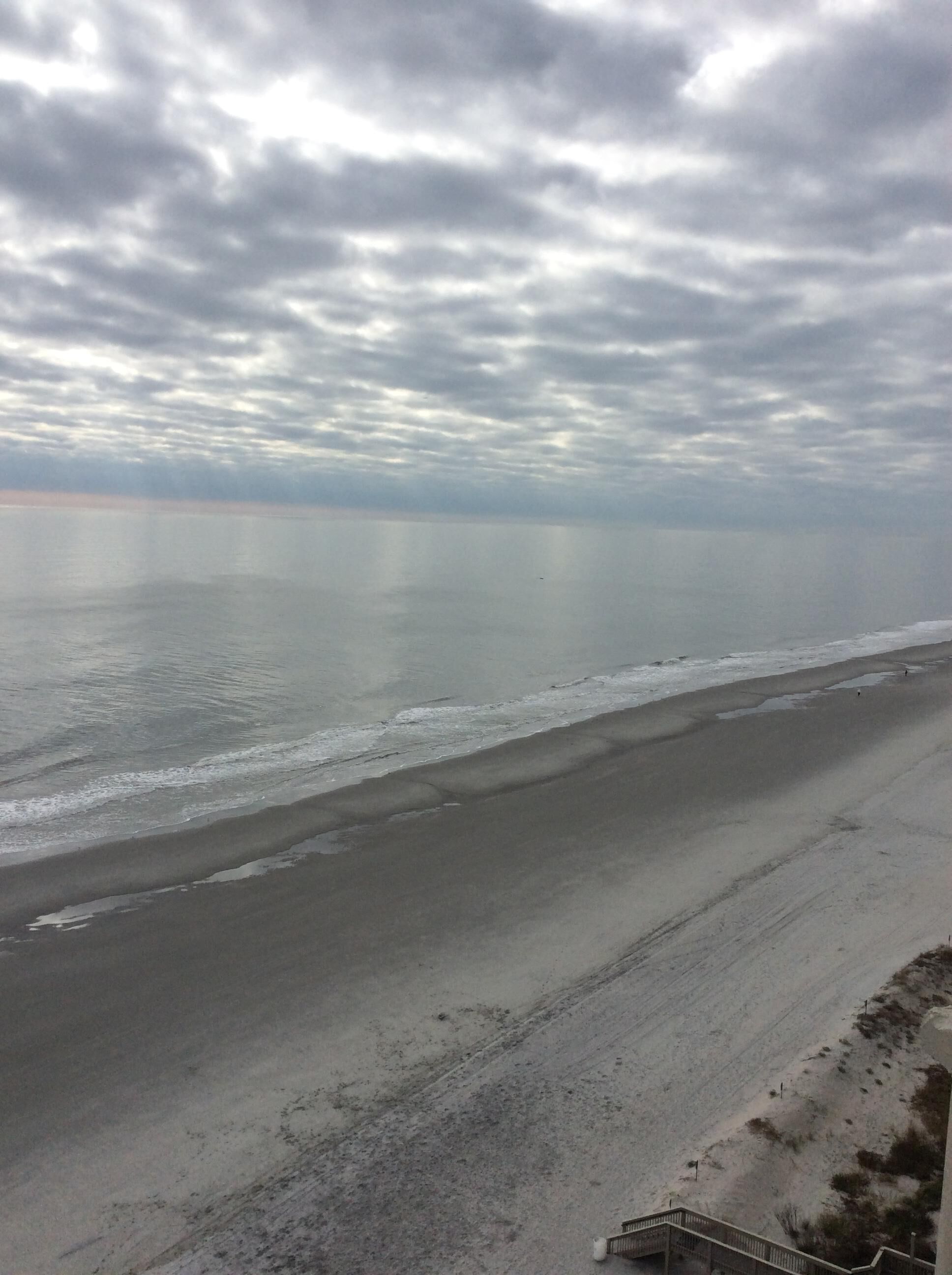 Ein Strand mit einer Treppe, die zum Ufer führt, ruhigem Meer und bewölktem Himmel.