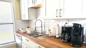 A kitchen with white cabinets, a wooden countertop, a stainless steel sink, a coffee maker, and a paper towel dispenser.