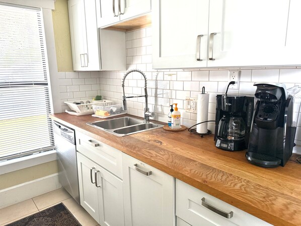 A kitchen with white cabinets, a wooden countertop, a stainless steel sink, a coffee maker, and a paper towel dispenser.