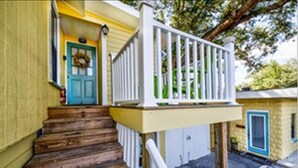 A wooden staircase leading to a porch with a white railing, a blue door, and a small porch area with a white fence.