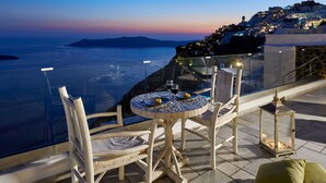 A table with chairs and a lantern on a terrace overlooking a coastal city at dusk. - Luxury Cave Villa, Caldera View, Outdoor Heated Plunge Pool (Imerovigli, Thira)