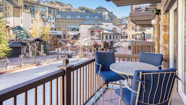 Un balcone con sedie blu e un tavolo, con vista su una cittadina con edifici e una seggiovia.