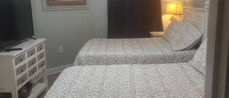 Een slaapkamer met twee bedden, een televisie op een nachtkastje, een schilderij aan de muur en een plafondventilator.