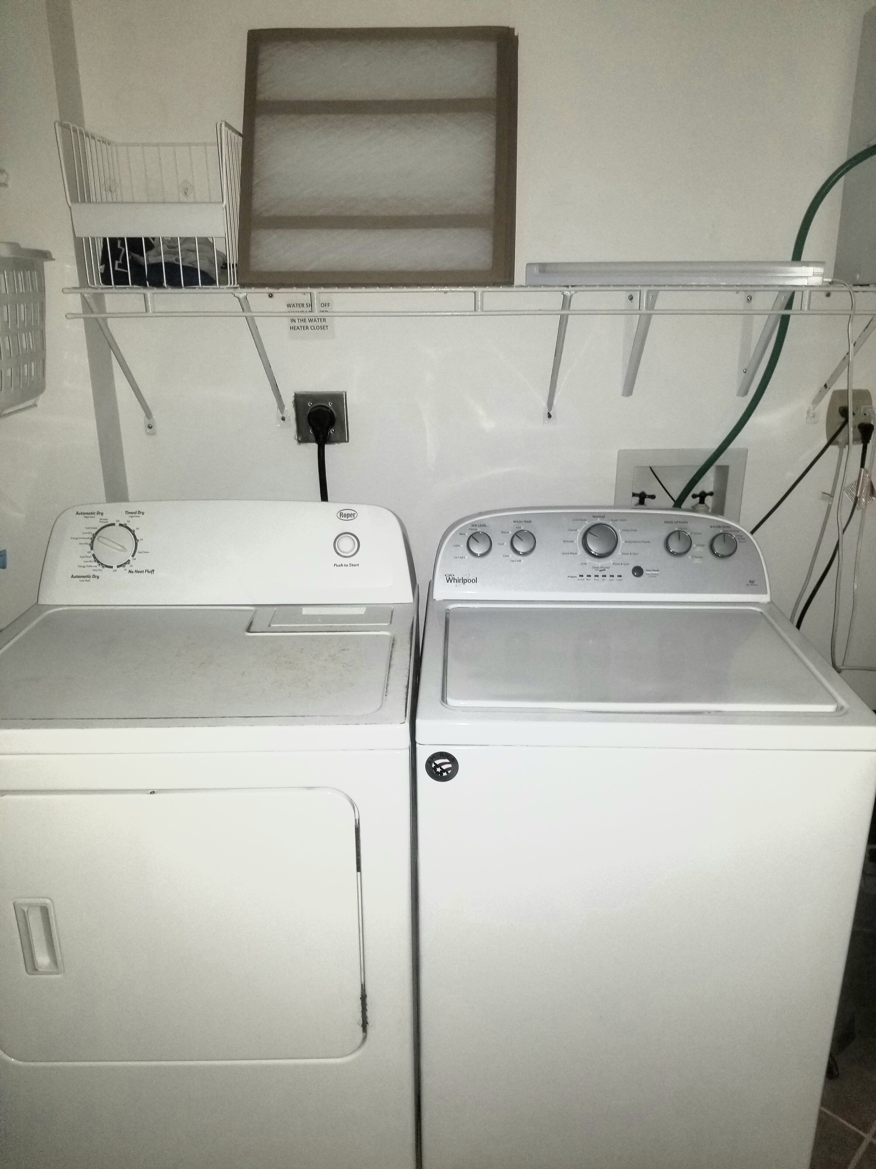 Ein Waschraum mit zwei weißen Whirlpool-Waschmaschinen, einer Steuerung mit verschiedenen Einstellungen und einem Wasserzulauf/Abfluss.