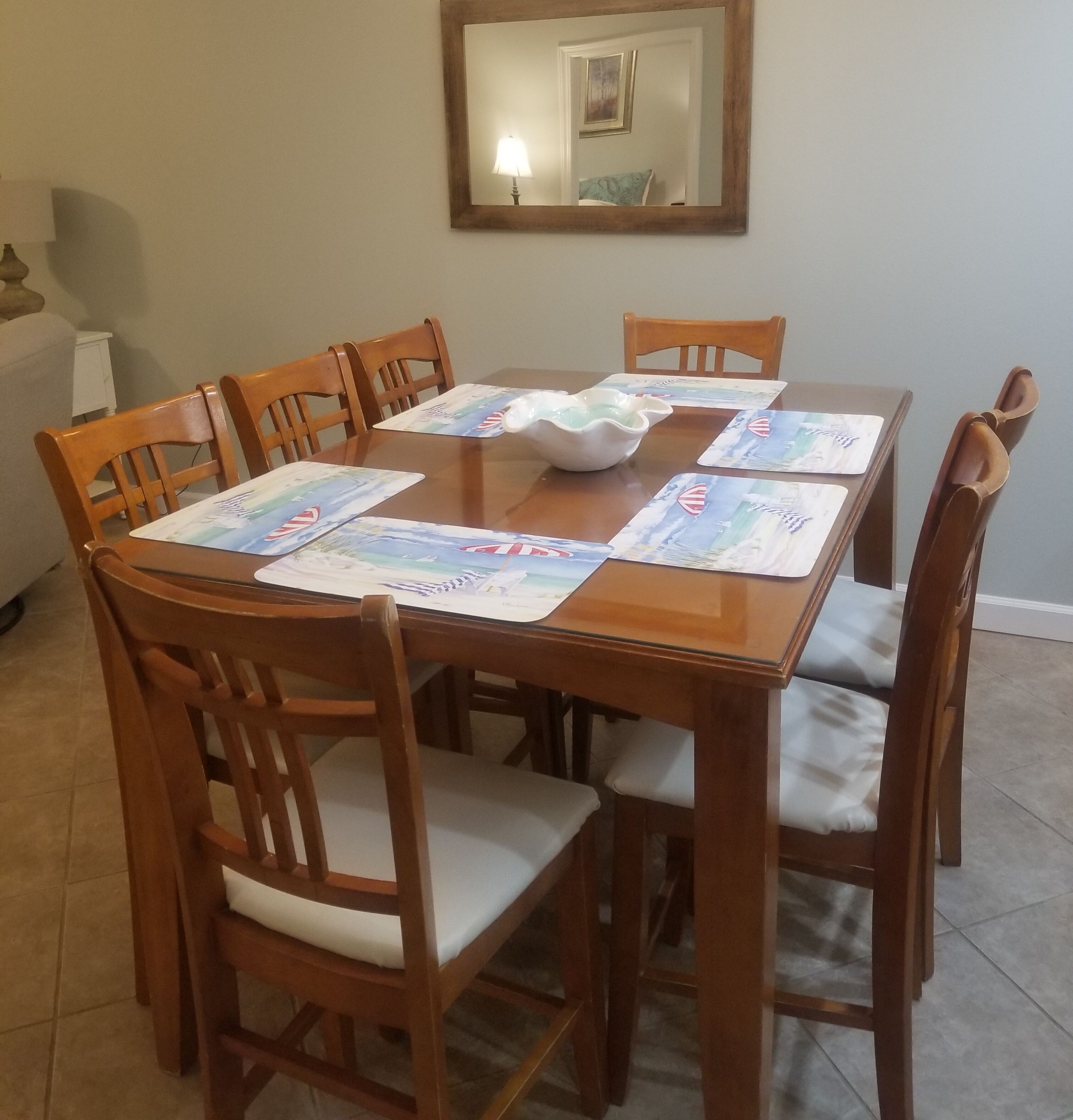 Una mesa de comedor con sillas de madera, un tazón blanco y manteles individuales con motivos náuticos.