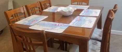 Una mesa de comedor con sillas de madera, un tazón blanco y manteles individuales con motivos náuticos.