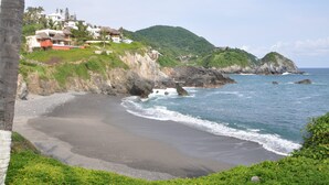Eine Küstenlandschaft mit sandigem Strand, felsigen Klippen und einer Hanglage mit Gebäuden.