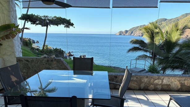 Eine Terrasse mit Glastisch und Stühlen mit Blick auf das Meer.