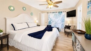 Quarto de hotel com cama, escrivaninha, cadeira, televisão e ventoinha no teto.