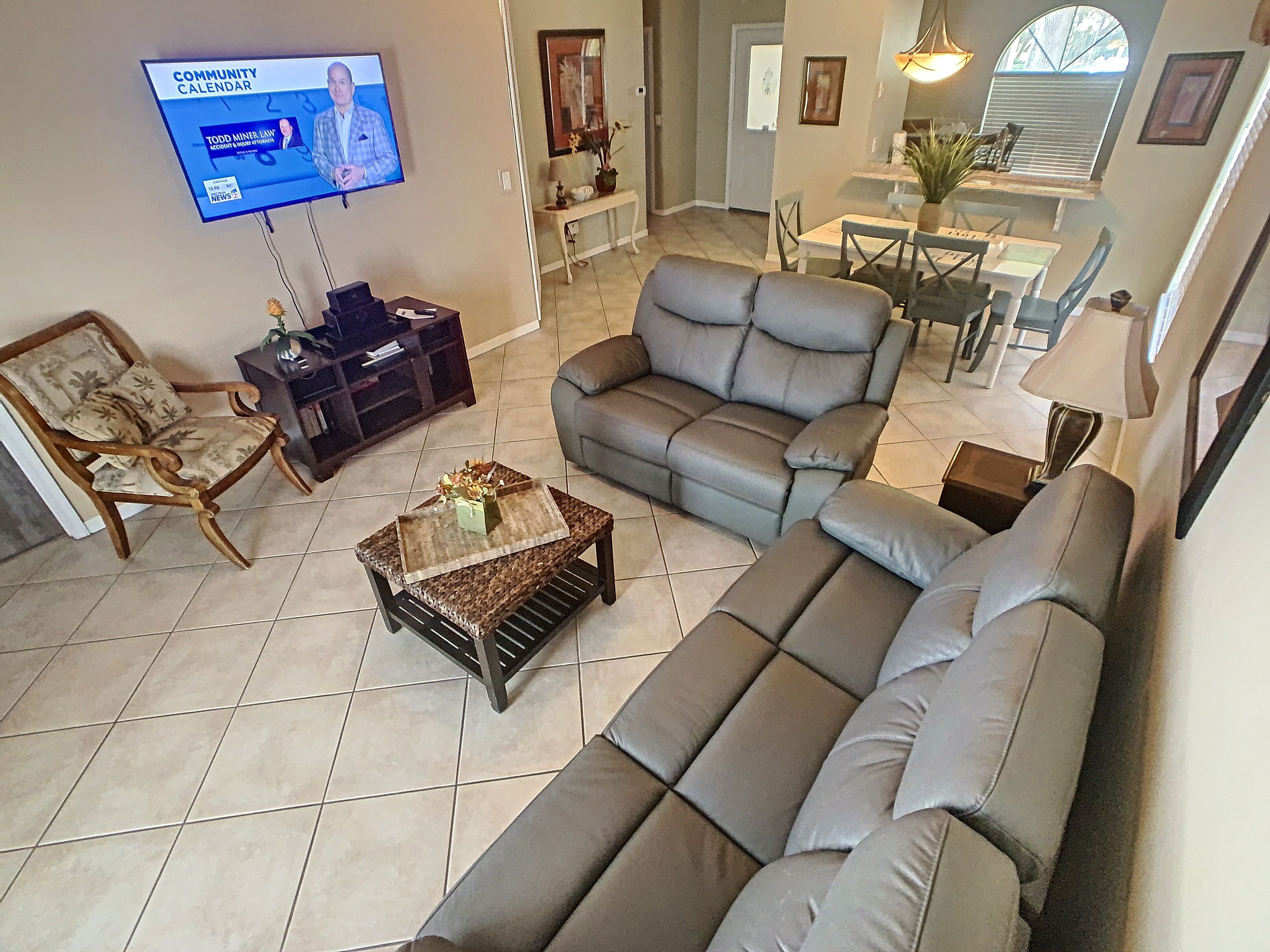 A living room with a sofa, a chair, a coffee table, and a television displaying a community calendar.