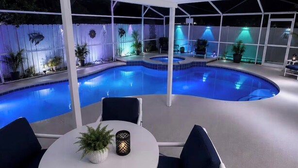 Piscina interna com área de estar coberta, plantas em vasos e iluminação ambiente.