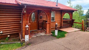 Une cabane rustique en bois, avec un toit en métal rouge, une véranda en bois et un paillasson.