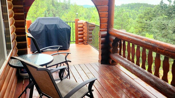Une terrasse en bois dotée d’un espace barbecue couvert, de sièges d’extérieur et offrant une vue sur un paysage boisé.