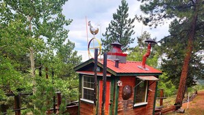 Une petite cabane avec un toit rouge, une cheminée et un coq décoratif sur le sommet.