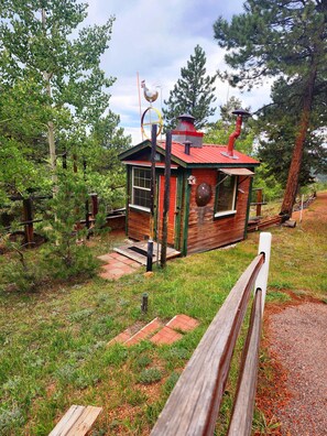 A small cabin with a red roof, a chimney, and a rooster decoration on top.