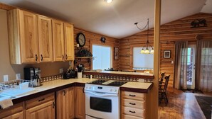 Une cuisine de style rustique, avec des murs en bois, un îlot central, des armoires en bois, une cuisinière et une horloge au mur.