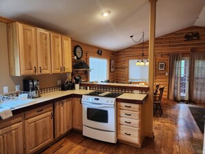 A wooden cabin-style kitchen with a central island, wooden cabinets, a stove, and a clock on the wall.