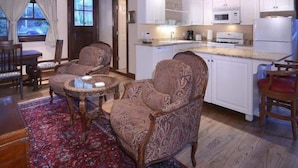 Uma sala de estar ampla com poltronas estampadas, uma mesa de jantar e uma cozinha com armários e eletrodomésticos brancos.