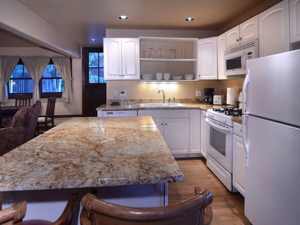 A kitchen with granite countertops, white cabinets, a built-in microwave, and a refrigerator.