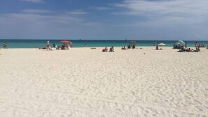 Une vaste plage de sable, avec des parasols et des gens.