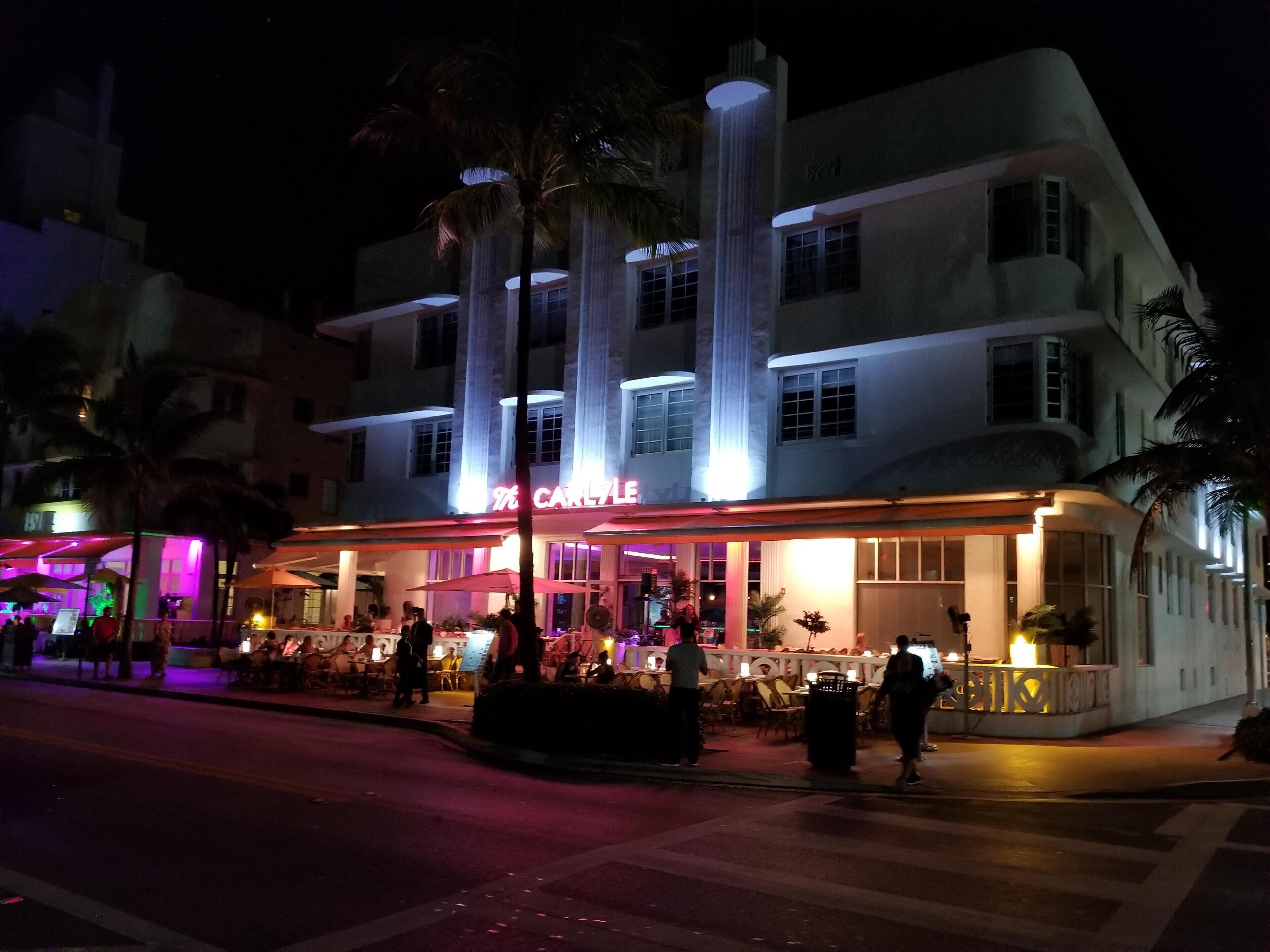 Um hotel com vários andares, um letreiro chamativo, área de estar externa e palmeiras.