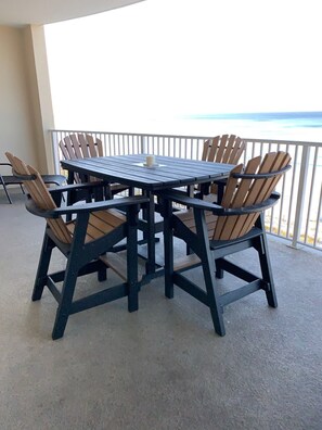 A round table with six wooden chairs on a balcony with a view of the ocean.