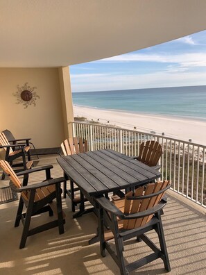 A balcony with a wooden table and chairs, overlooking a beach.