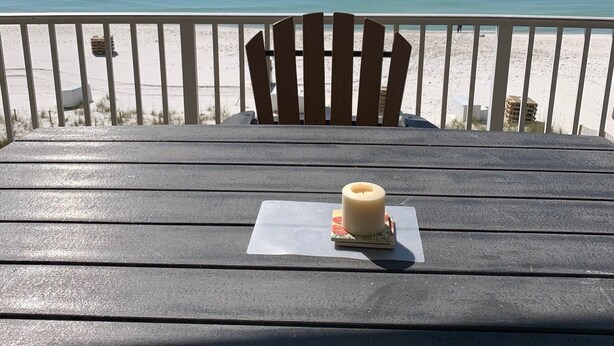 Una terraza de madera con una silla y una vela sobre una mesa, con vistas a la playa y al océano.