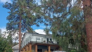 A modern two-story house with a stone foundation, wooden beams, and a balcony with potted plants. - Cozy house in the shade of pines with Lake and Mountain view (Kelowna)