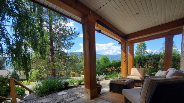 A covered outdoor seating area with a view of trees and mountains. - Cozy house in the shade of pines with Lake and Mountain view (Kelowna)