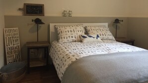 A bedroom with a bed, two bedside tables, a wall clock, a motivational sign, and a small shelf with jars. - Cozy house in the shade of pines with Lake and Mountain view (Kelowna)