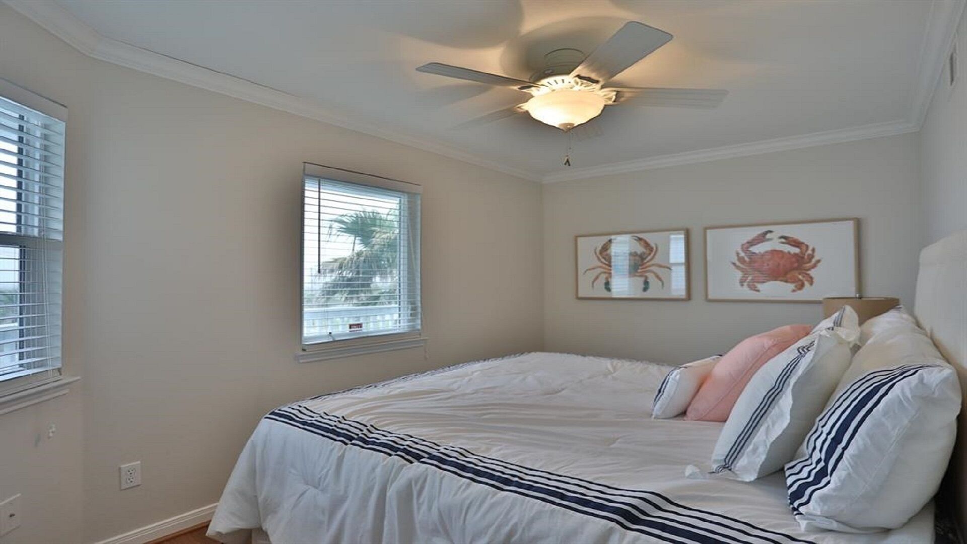 A bedroom with a bed, ceiling fan, window, and two framed pictures on the wall.