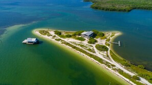 Vue aérienne d’une propriété située sur la côte, avec un bâtiment principal, un quai et un bateau.