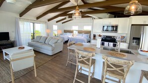 A modern, open-plan living and dining area with a kitchen, wooden beams, and large windows. - North Captiva Point House - Boat/Water Taxi Only **NEWLY RENOVATED ** (North Captiva)