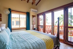 Une chambre à coucher comprenant un lit, une fenêtre, un climatiseur et un balcon avec des chaises et une table.