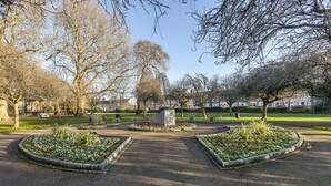 Un parc avec des parterres de fleurs circulaires, des bancs et des arbres.