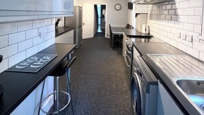 Une cuisine moderne avec des armoires blanches, un comptoir noir et un four encastré. On y trouve un coin repas avec une table et des chaises, et une vue sur une autre pièce grâce à une porte ouverte.