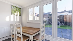 Un coin repas avec une table en bois et des chaises blanches, de grandes fenêtres et une vue sur le jardin.