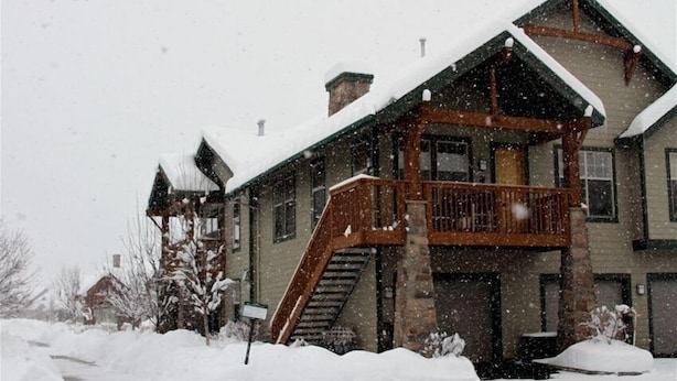 Een tweelaags lodge met een houten trap naar een balkon, omgeven door sneeuw.