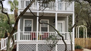 Una casa de dues plantes amb façana blanca, un porxo amb barana blanca i una tanca de fusta.
