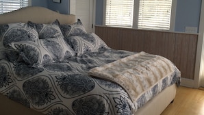 A bedroom with a bed, a window with blinds, and a door.