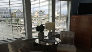 A room with two chairs, a table, and a lamp. There is a view of a marina through large windows.