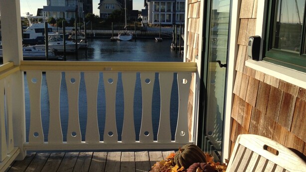 A wooden deck with a chair, overlooking a marina with boats and houses.