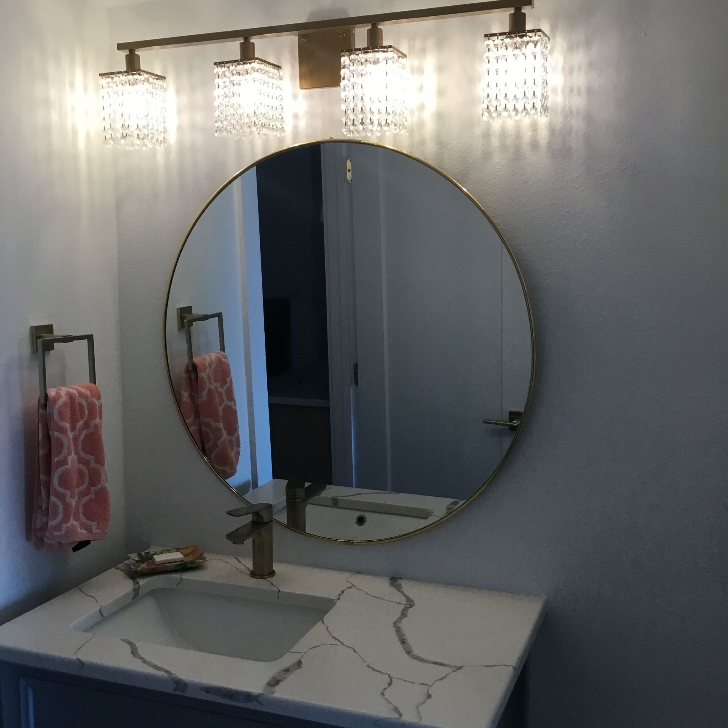 Une salle de bain avec un miroir rond, un lavabo doté d’un plan de toilette en marbre et un porte-serviettes avec des serviettes à motifs.