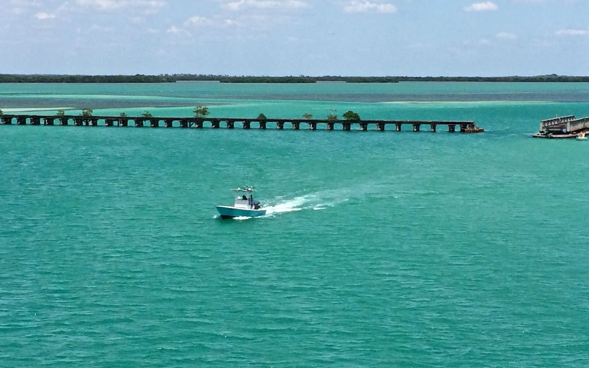 A boat moving across a turquoise sea with a pier extending into the water.