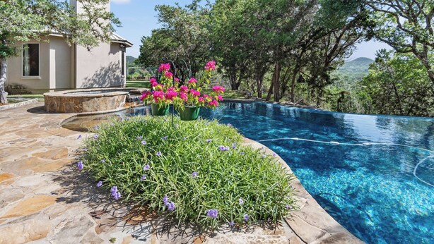 A swimming pool with a stone deck and flower beds, surrounded by trees and a building. - Rockin B Summit | Luxury Retreat with Pool & Creek (Pipe Creek)