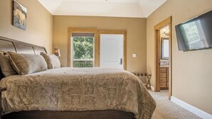 A bedroom with a large bed, a television mounted on the wall, and a door leading to a balcony. - Rockin B Summit | Luxury Retreat with Pool & Creek (Pipe Creek)